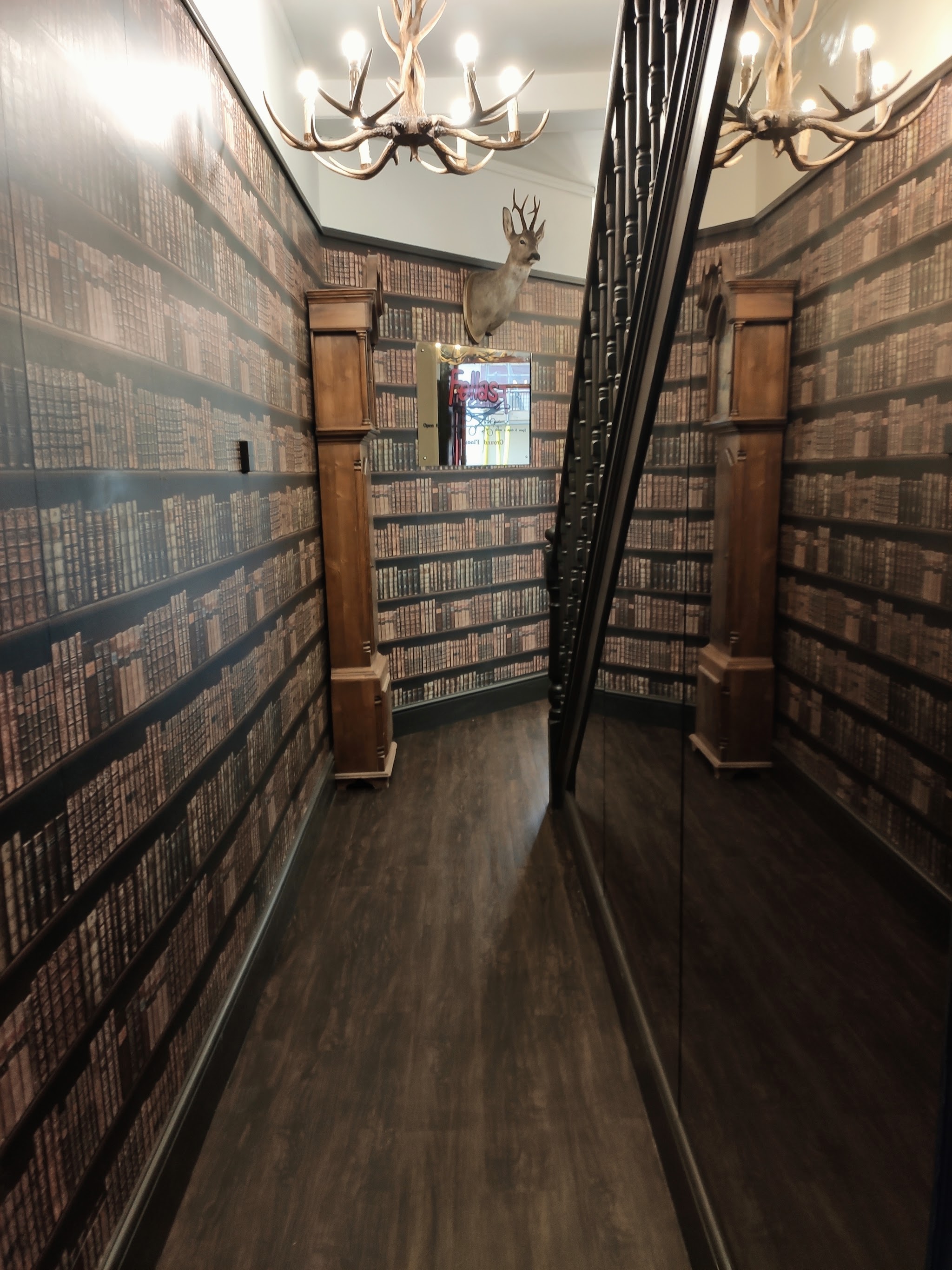 Corridor lined with library-bookshelf wallpaper under antler chandeliers