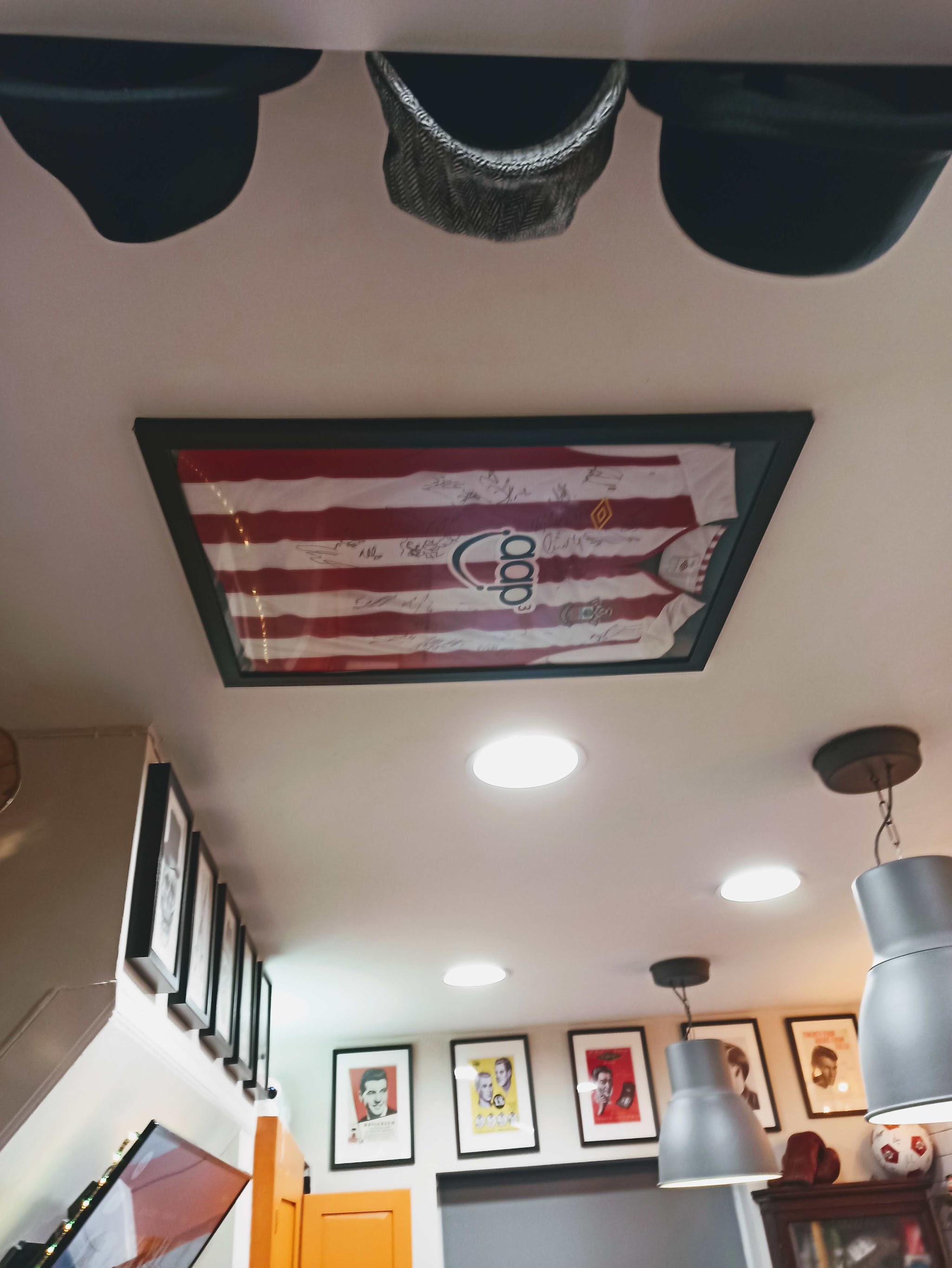 Framed red and white football shirt on the ceiling among pendant lamps