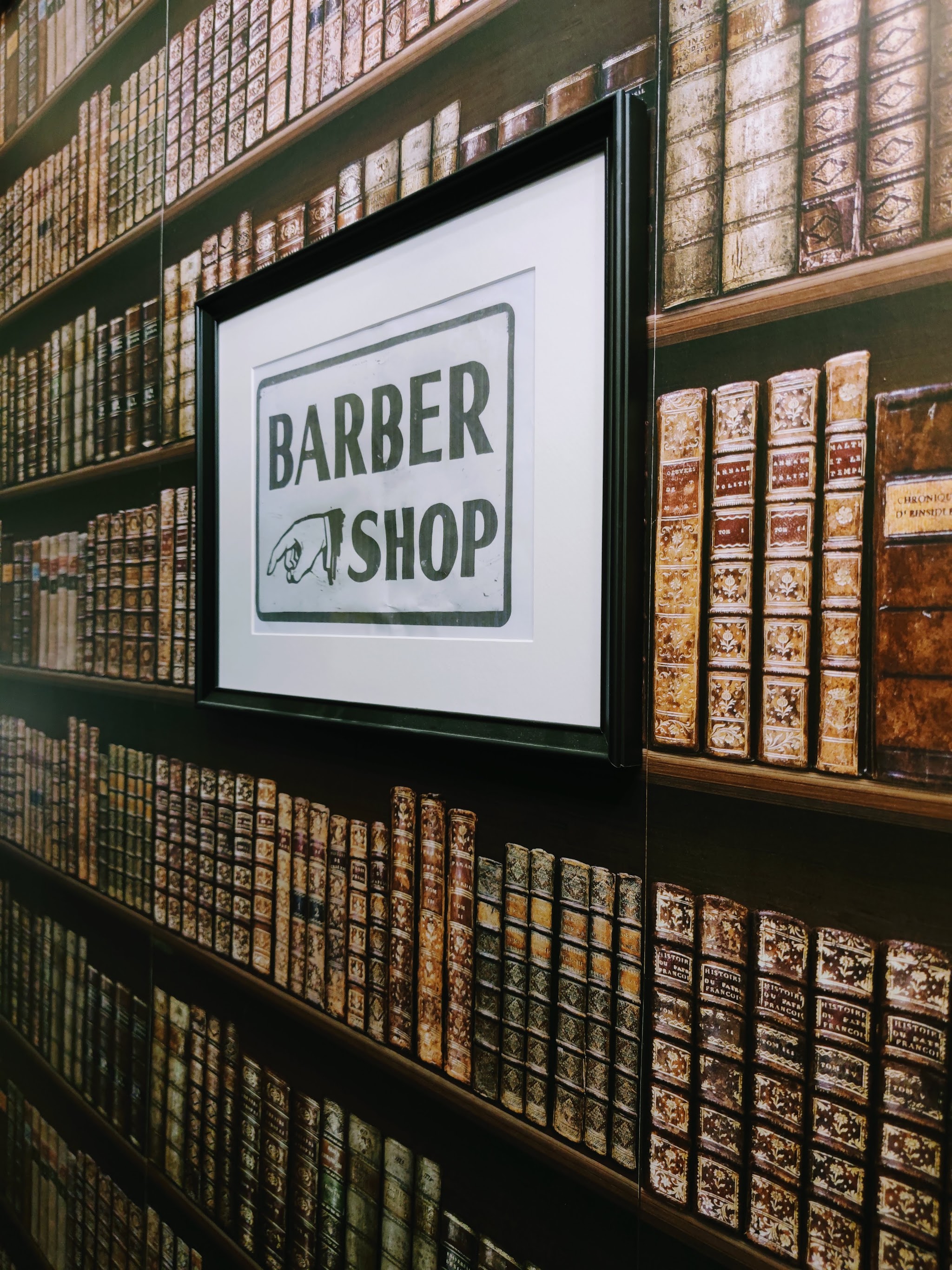 Framed Barber Shop sign hanging on the bookshelf wallpaper